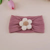 A mauve knitted elastic baby headband with a white floral appliqué on a light pink background.