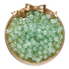 A round gold-toned dish filled with small, translucent green glass crackle beads for jewelry making