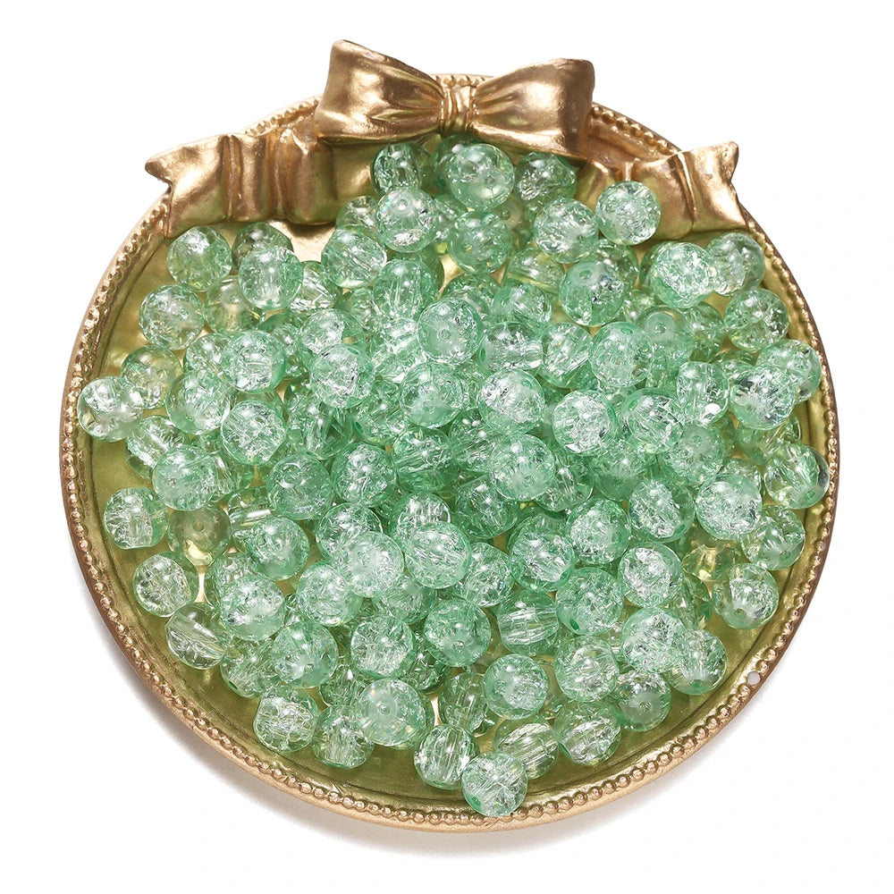 A round gold-toned dish filled with small, translucent green glass crackle beads for jewelry making