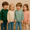 Four children wearing pastel colored pullover hoodies standing together outdoors