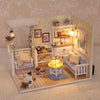 A miniature dollhouse kit featuring white furniture, decor, and a kitten figure set within a light-colored room scene.