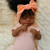 A lifelike 19-inch reborn baby doll with hand-rooted hair is lying on a fluffy white surface.
