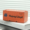 An orange industrial storage box labeled Hapag-Lloyd resting on a white book.