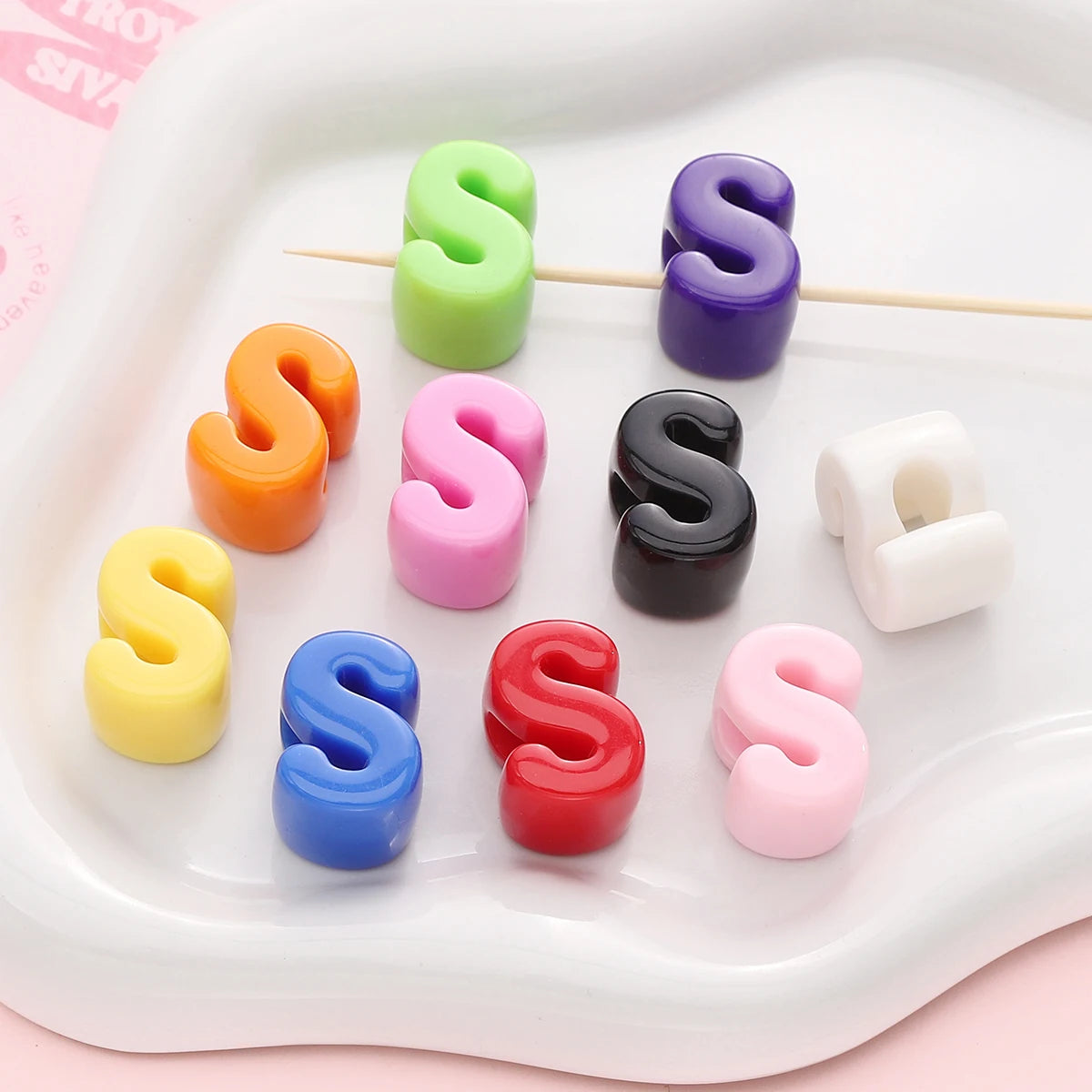 A collection of colorful acrylic letter beads in various shades of green, purple, orange, pink, yellow, and blue arranged on 