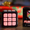 A black musical brain teaser cube with flashing lights resting on a wooden surface.