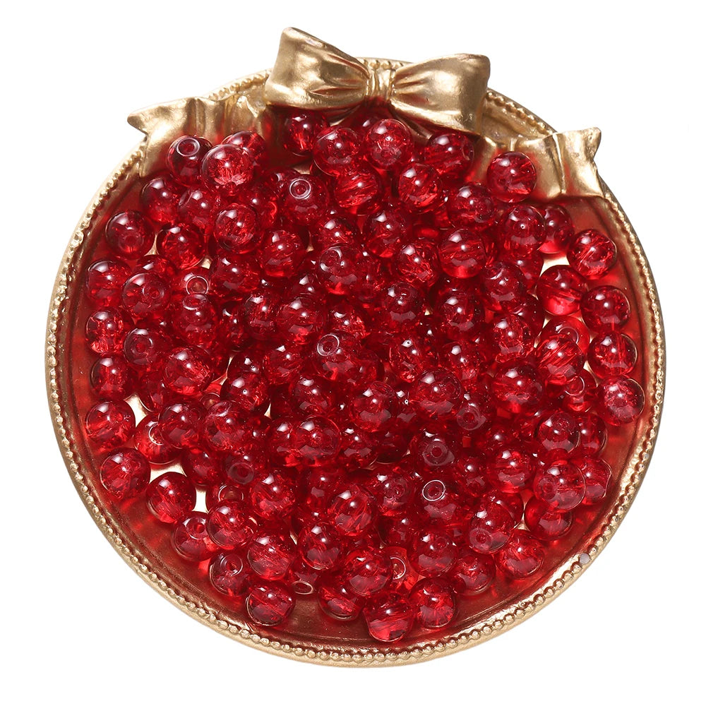 A round gold-rimmed dish filled with bright red glass crackle beads for jewelry making
