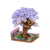 A miniature tree built from building blocks featuring purple blossoms and a small house structure.