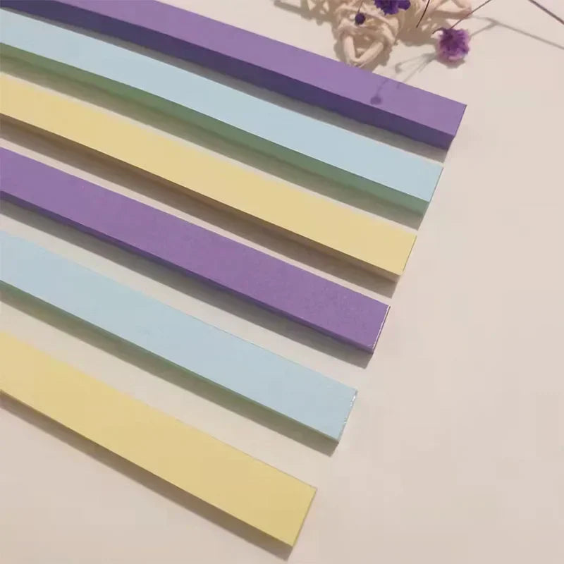 A collection of purple, blue, and yellow rectangular origami star strips laid diagonally on a white surface.