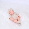 A realistic soft vinyl baby doll with a newborn outfit set lying on a white surface.