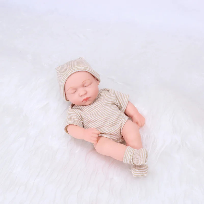 A realistic soft vinyl baby doll with a newborn outfit set lying on a white surface.
