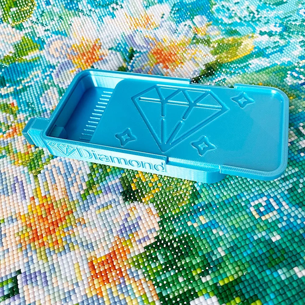 A light blue diamond painting organizer tray with storage compartments placed on a colorful fabric background.