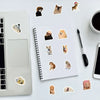 A spiral notebook filled with various funny dog stickers placed on a white desk next to a silver laptop.