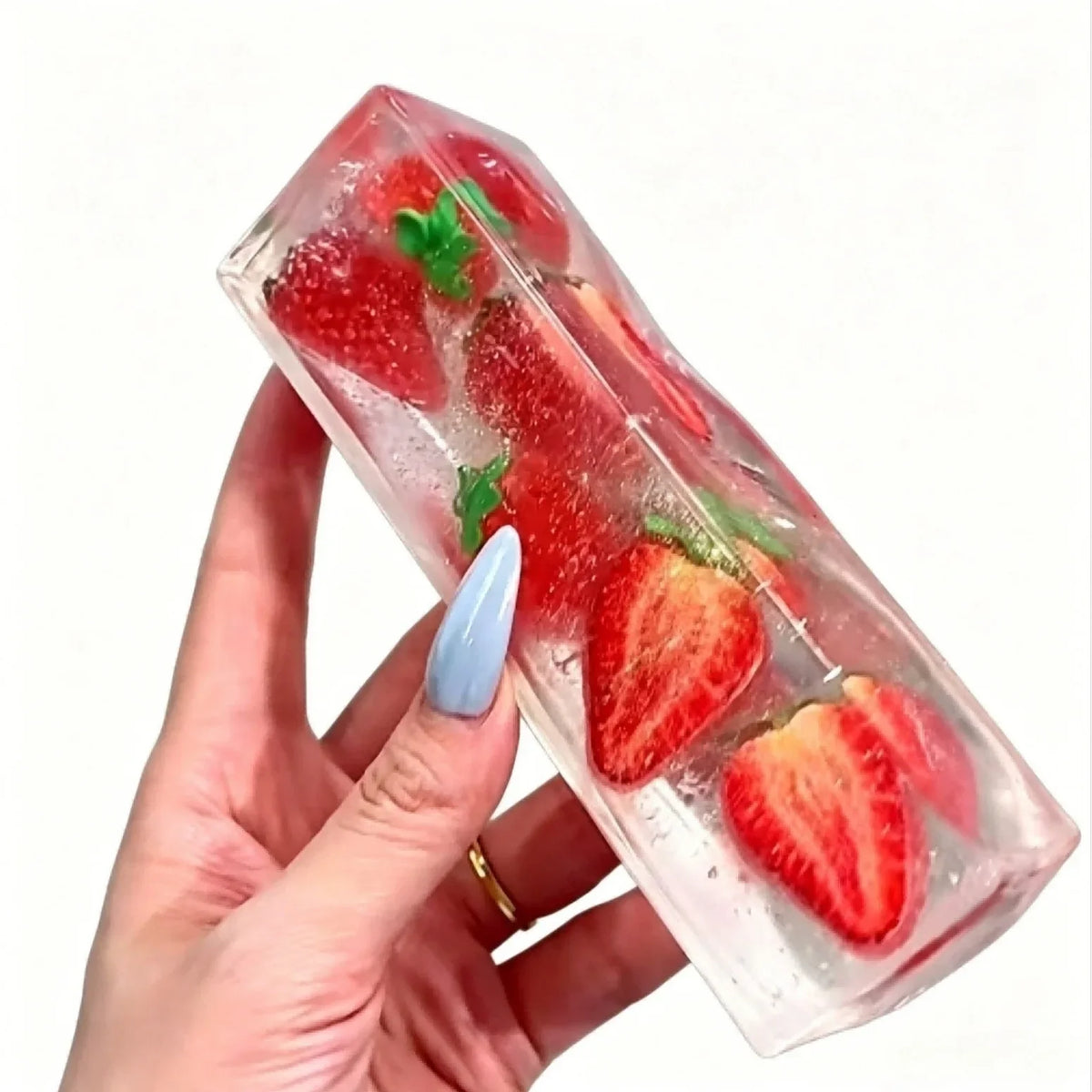 A hand holds a clear ice cube shaped like a strawberry, used as a squishy stress relief toy.
