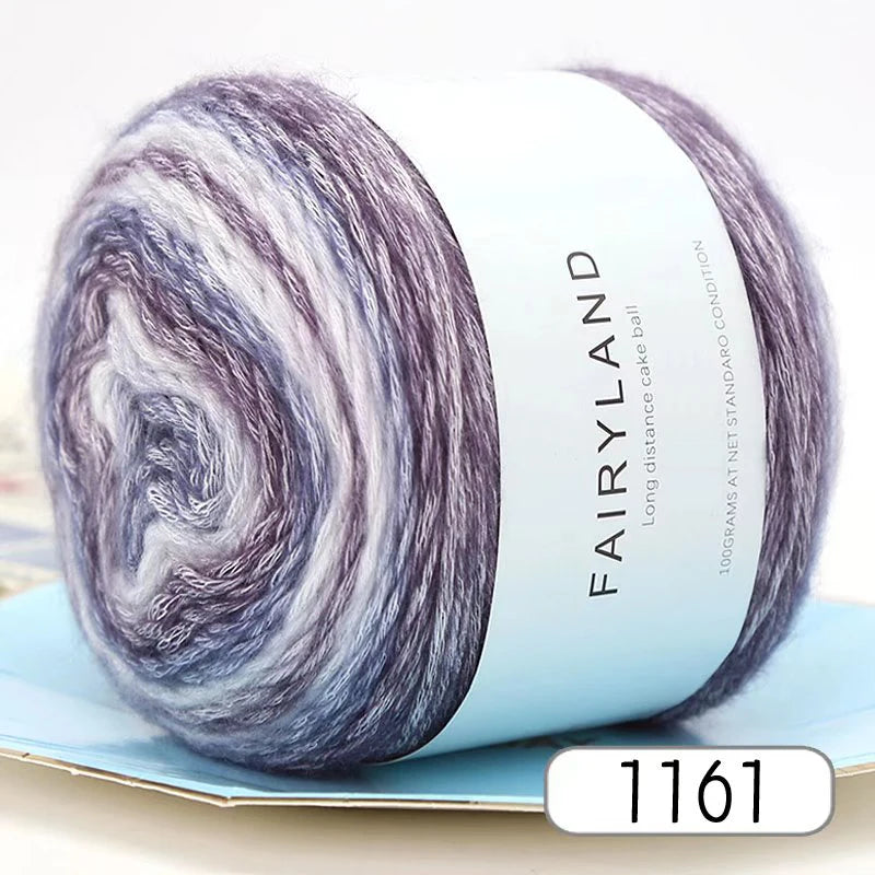 A ball of silky gradient yarn in shades of purple and gray resting on a light blue surface.