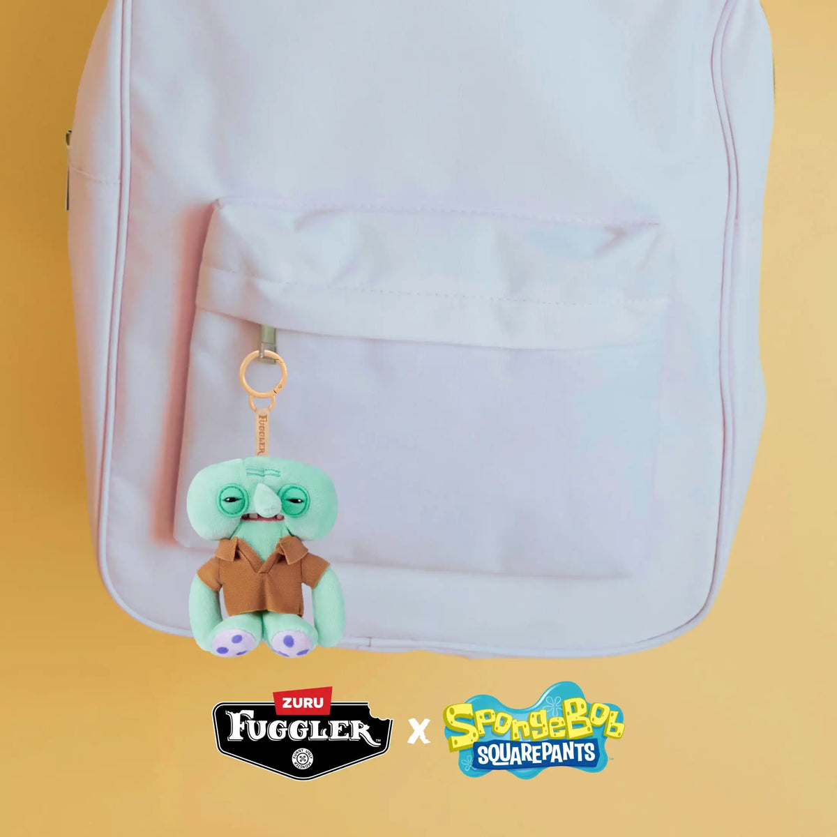 A light pink backpack with a pocket featuring a green plush monster keychain.