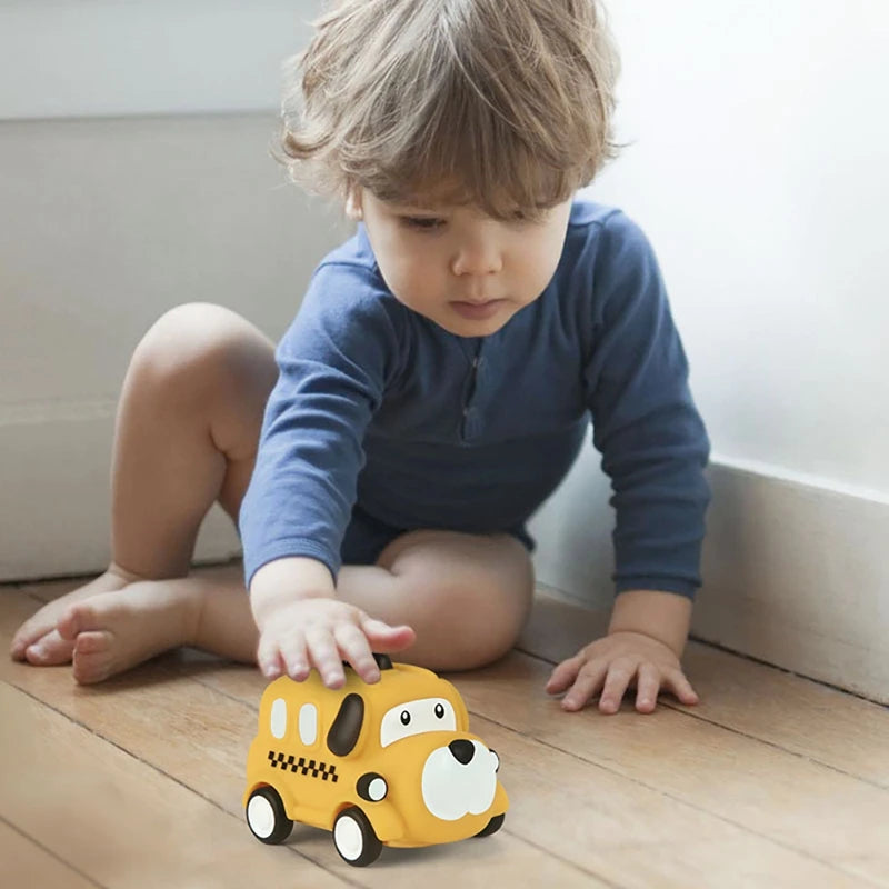 A young child is looking down at a yellow pull-back toy car on a wooden floor.