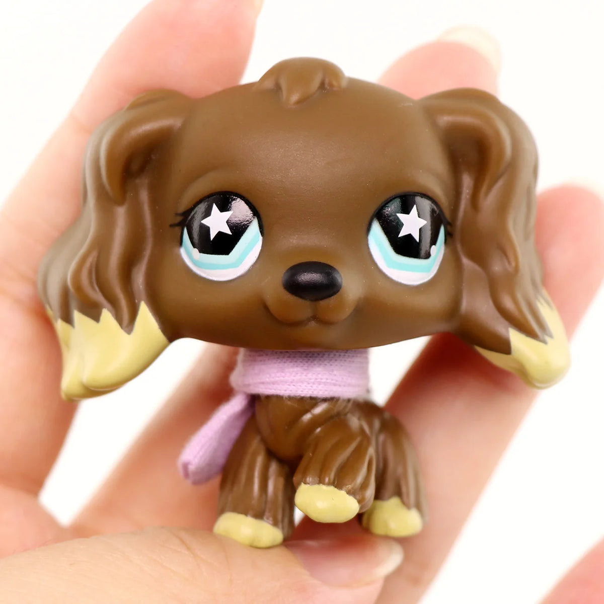 A small brown dog figure with floppy ears and light blue eyes is held in a person's hand.