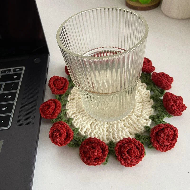 Hand-crocheted red and green lily of the valley coasters with a glass cup.