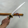 A hand holds a silver katana prop with a wooden hilt and purple cord, resting on an orange stick.