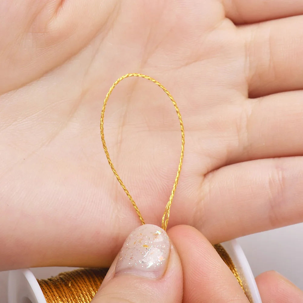 A hand holds a thin gold metallic craft cord for jewelry making, demonstrating the material.
