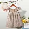 A beige floral smocked summer dress for girls with puff sleeves hanging on a wooden hanger.