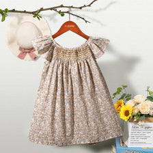A beige floral smocked summer dress for girls with puff sleeves hanging on a wooden hanger.