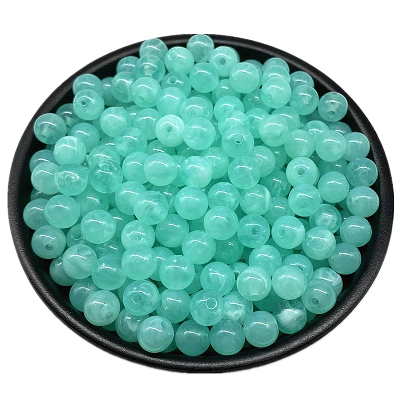 A pile of light aqua clear acrylic round beads for jewelry making in a black bowl.