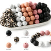 A collection of soft food-grade silicone beads in various colors including black, white, peach, and pink, displayed on a whit