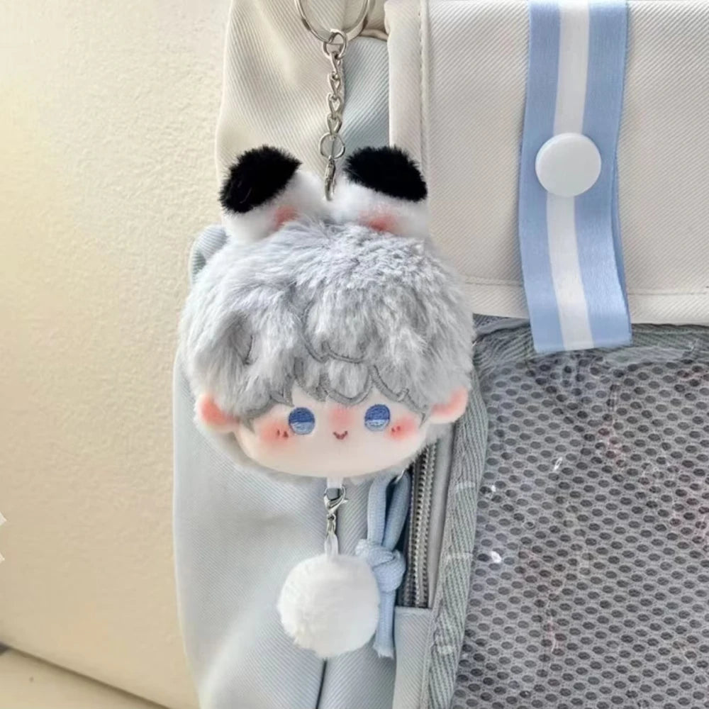 A cute white and gray plush pendant keychain featuring rabbit ears and blue eyes, suspended from a light blue fabric strap.