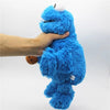 A hand is holding a bright blue Cookie Monster plush toy with a white nose against a white background.