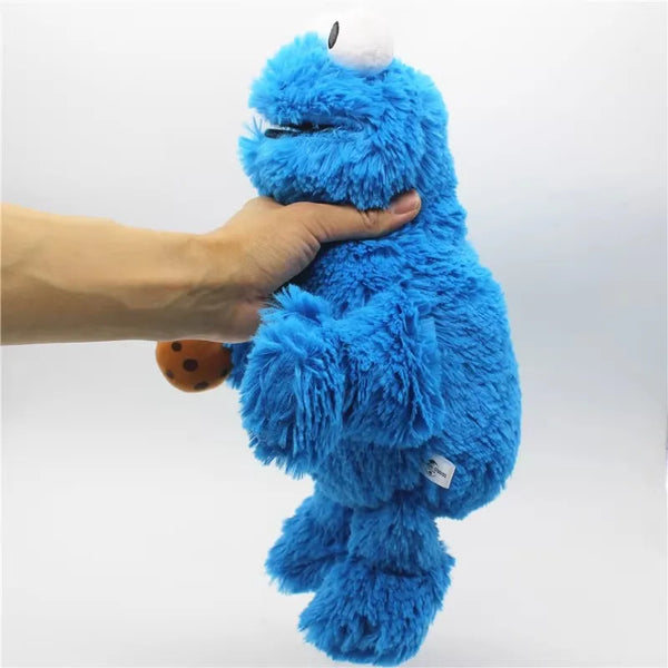 A hand is holding a bright blue Cookie Monster plush toy with a white nose against a white background.