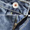 Close-up of dark blue denim jeans showing a metal button and a zipper detail.