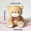 A light beige seated bear figure with a pink bow, measuring 5.5cm high.