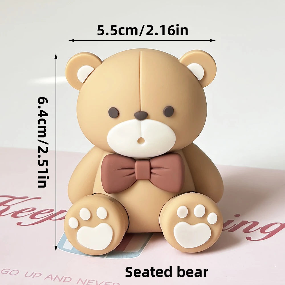A light beige seated bear figure with a pink bow, measuring 5.5cm high.