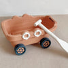 A pink kids sand and water play set featuring a pull-along bulldozer trolley with wooden wheels and a white shovel.