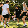 Three young people are playing soccer outdoors with a set of handmade crochet hacky sack balls.