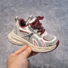 A close-up shot of a pair of pink and gray breathable mesh kids running sneakers with a cushioned sole being held by a hand.