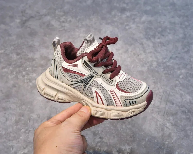 A close-up shot of a pair of pink and gray breathable mesh kids running sneakers with a cushioned sole being held by a hand.