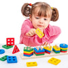 A toddler is holding a yellow wooden geometric shape puzzle piece while surrounded by various colored wooden shapes.