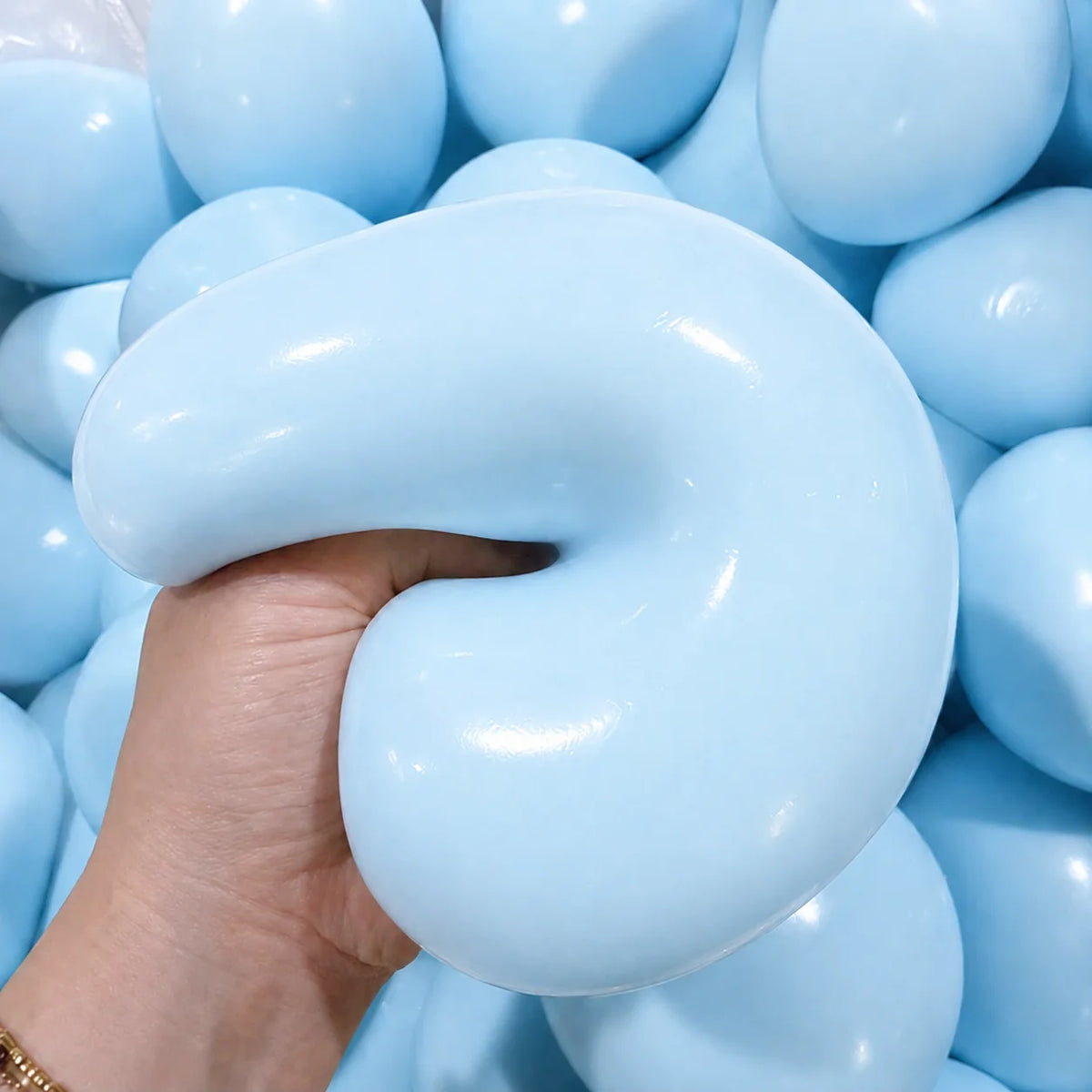 A hand is squeezing a light blue slow rising squishy ball stress relief fidget toy surrounded by many similar balls.