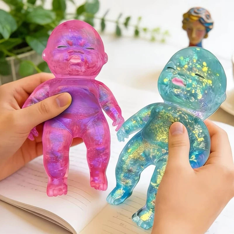Hands hold two squishy baby stress relief toys, one pink and one blue, on a notebook.