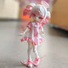 A white and pink articulated ball-jointed doll with pink hair and frilly clothing standing on a light surface.