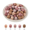A collection of 15 hexagonal silicone beads in various dusty rose and nude shades arranged on a white plate.