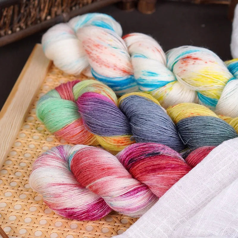 A collection of hand-dyed Australian wool yarn in various gradient colors, rolled and displayed on a woven mat.