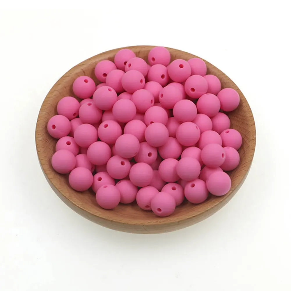 A wooden bowl filled with numerous small, round pink silicone beads for jewelry making and crafts.