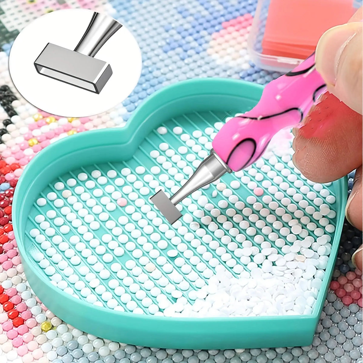 A pink diamond art pen set with interchangeable tips is shown dipping into a tray of white beads on a light blue background.
