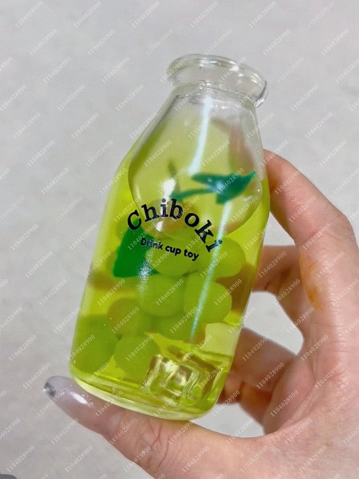 A hand holds a clear bottle filled with green squishy milk cup toys labeled Chiboki.