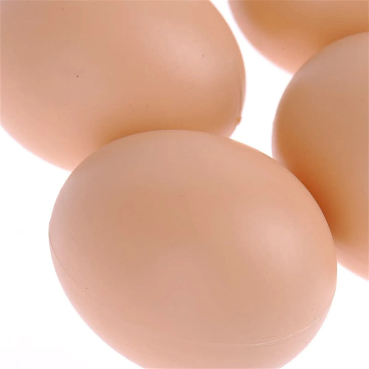A close-up view of several realistic, smooth, light peach colored plastic hen nesting eggs.
