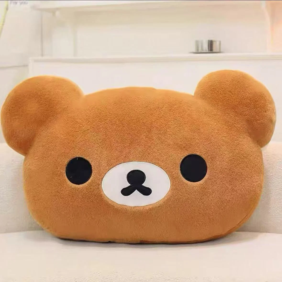 A soft, brown Rilakkuma plush hand rest pillow with black eyes and a white nose.