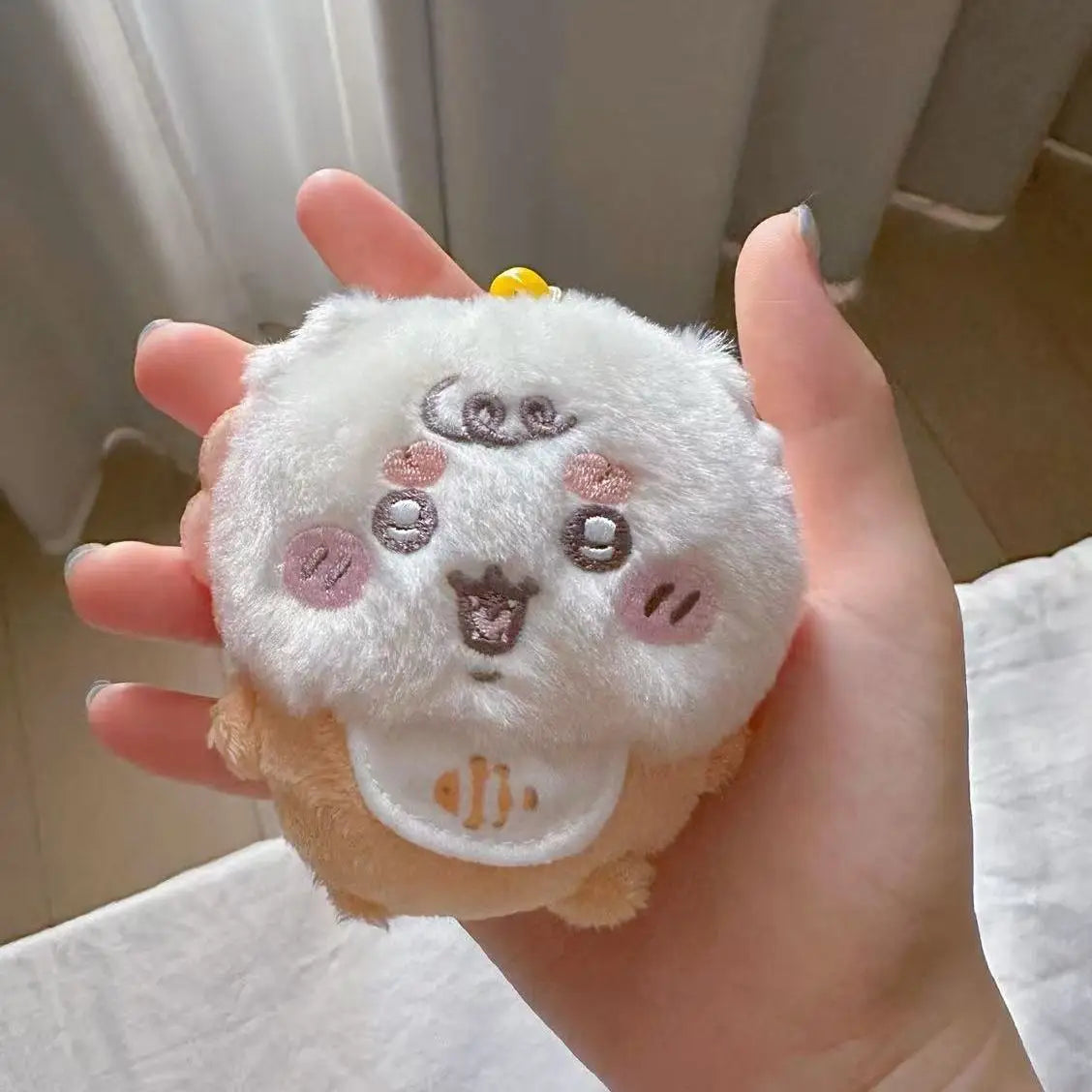 A hand holds a white fluffy plush keychain set featuring three cute animal faces.